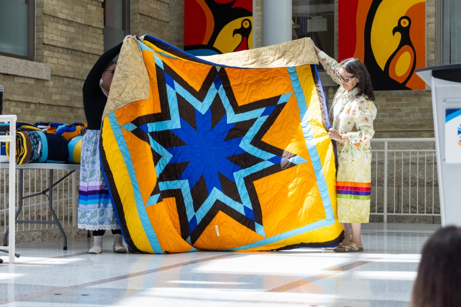 golden yellow and blue star blanket held by two women, being presented.