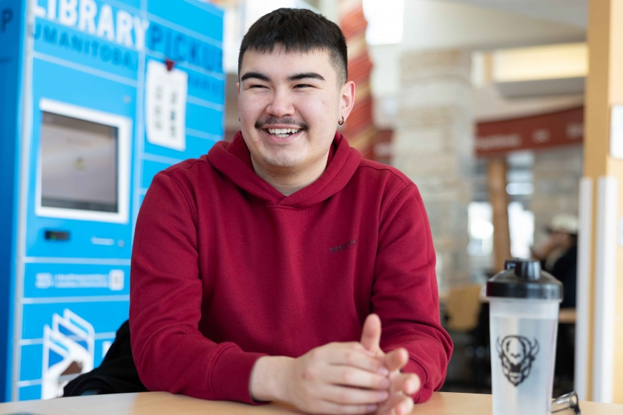 Male smiles candidly, seated at table wearing a red sweater.