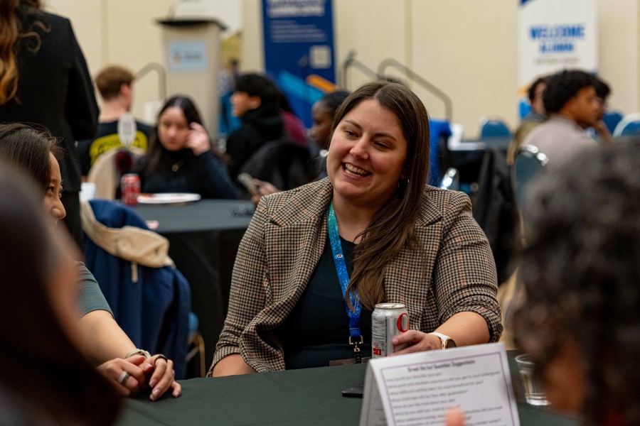 Woman sitting and chatting with students at a large table.