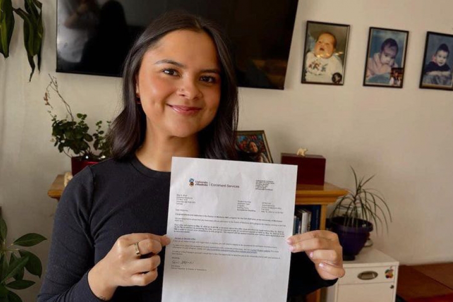 A woman holds up her medical school entry letter and smiles