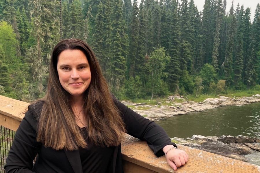 Cherie Murie stands on a bridge with a forest behind her.