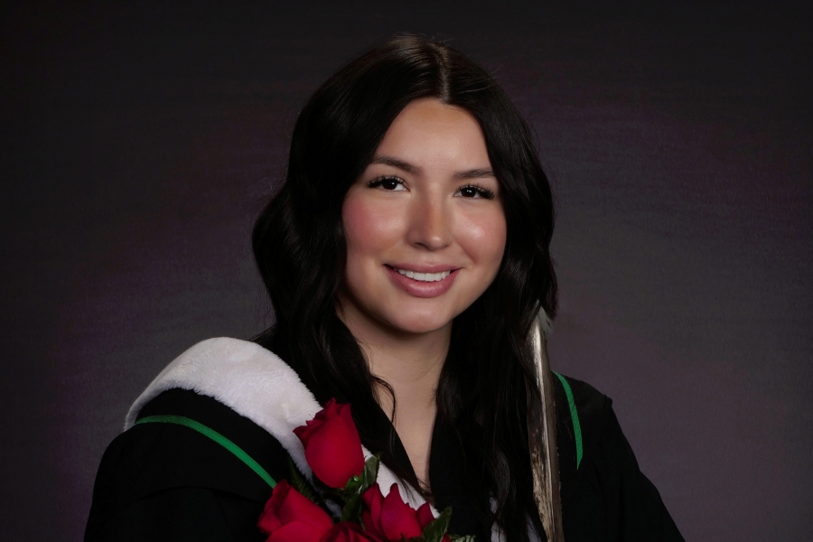 a woman in a graduation gown holds roses and smiles