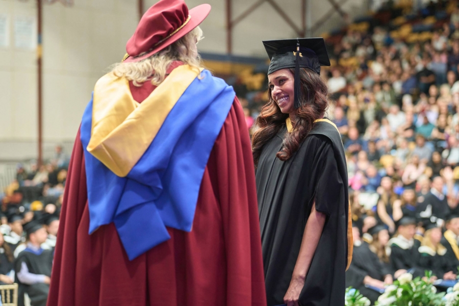 Student walking the procession line during UM Convocation ceremony is greeted by UM personnel on stage.