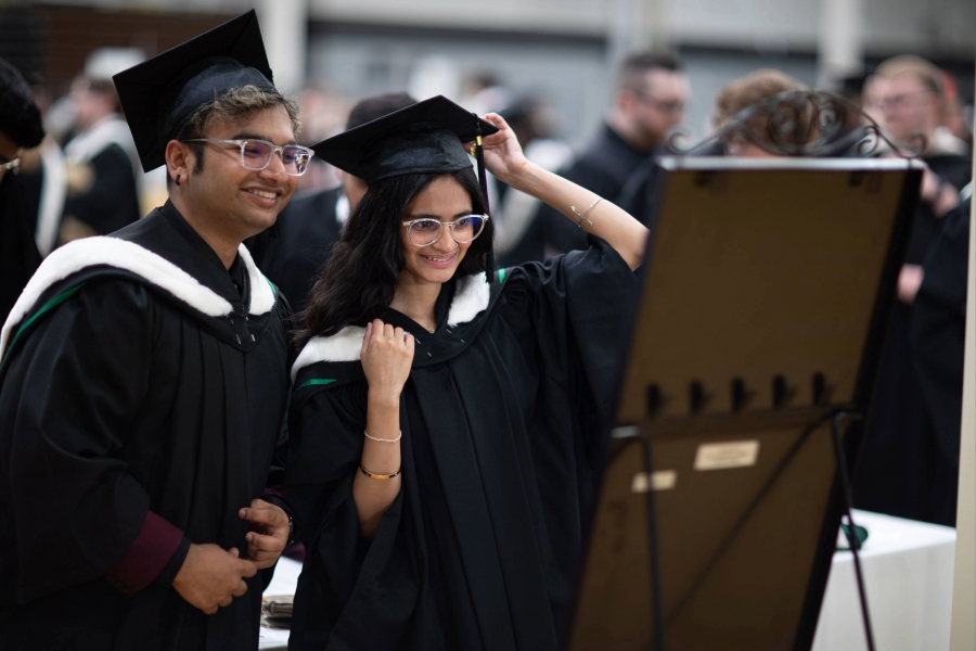 Two graduands looking in the mirror while getting ready at Convocation.
