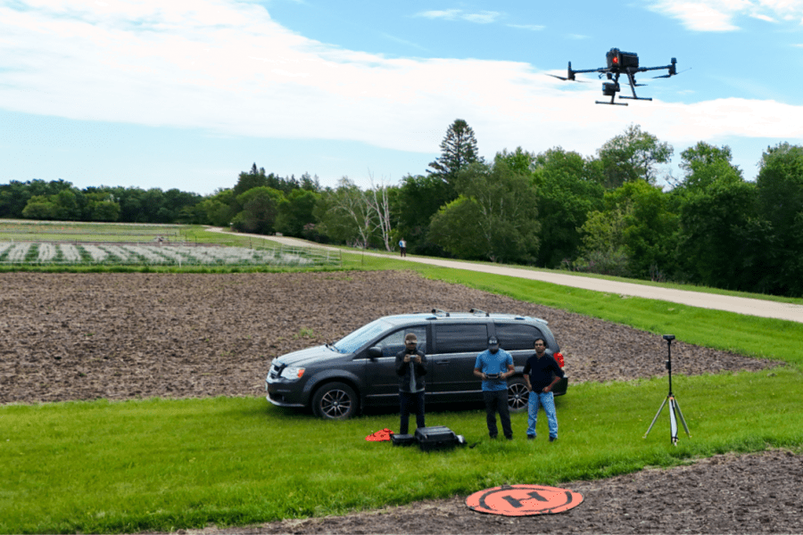 Three men stand outside in a field in front of a van.