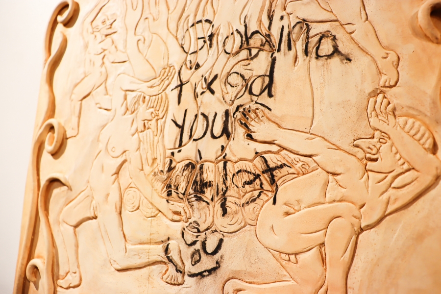 Ceramic relief sculpture featuring mythological figures and handwritten text.