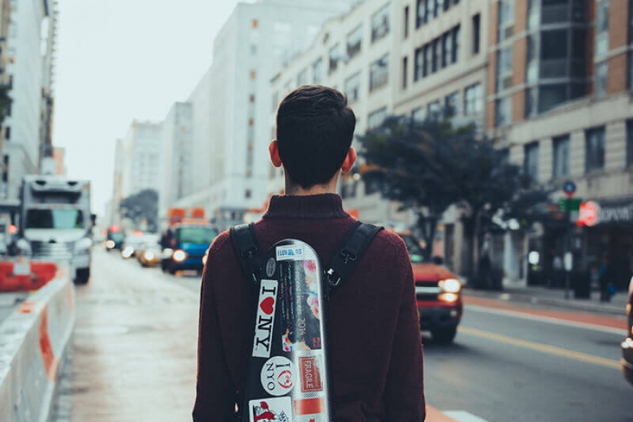 A young man standing on a street holding a violin case covered in stickers.