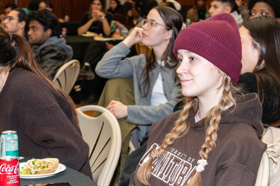 A student wearing a toque watching a performance on stage.