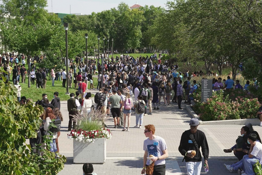 Students walk amidst green trees on the pedway, summer at Fort Garry campus.
