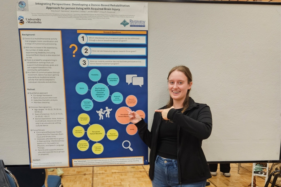 Abby Gooch smiling and pointing a her research poster