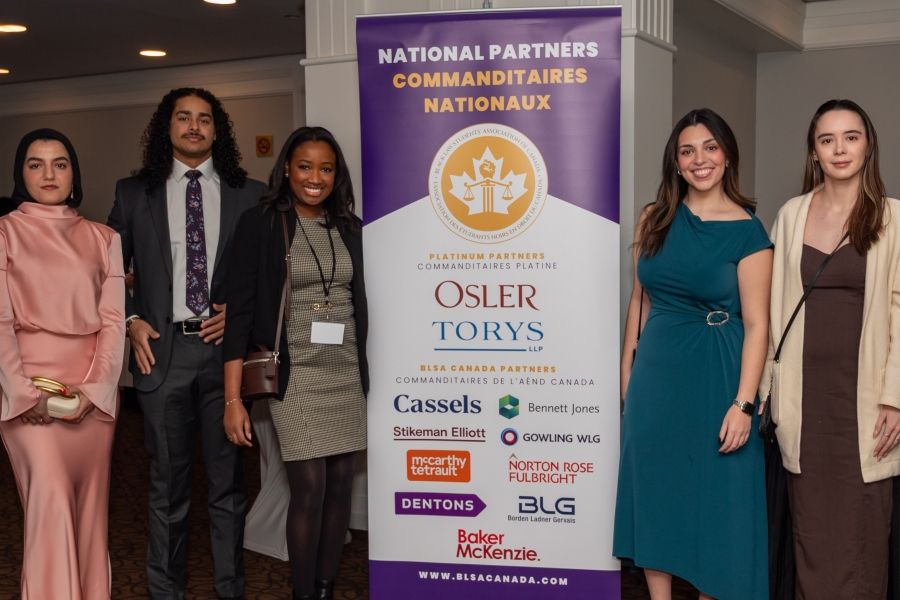 four law students and one moot team coach in formal wear pose in front of a roll up banner for the Black Law Students Association Isaac Moot sponsors
