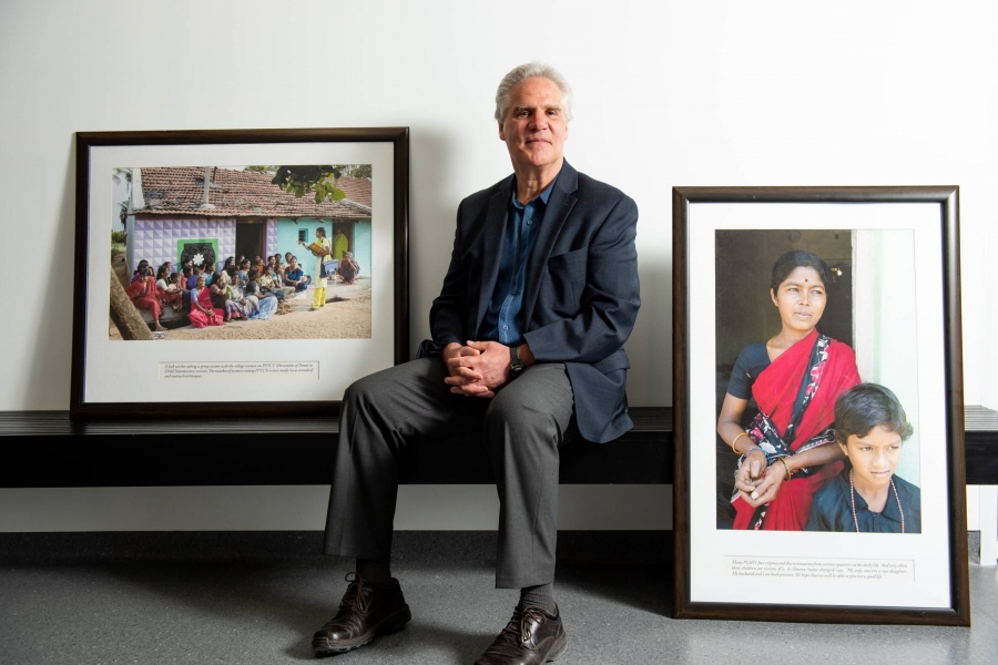 James Blanchard, Executive Director of UM's Global Institute of Public Health, sits on a bench, with a framed photos on either side