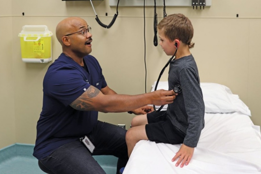 Dr. Jared Bullard and a child in an examination room. The child is wearing a stethoscope.