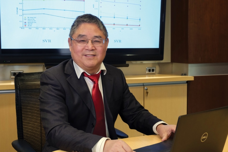 A researcher on his computer, behind is a screen with graphs.