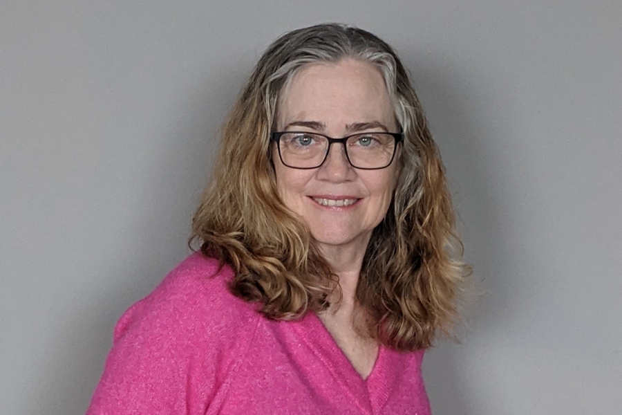 Karen Busby smiles facing the camera wearing a pink sweater. Her hair is shoulder-length blonde with grey at the temples.