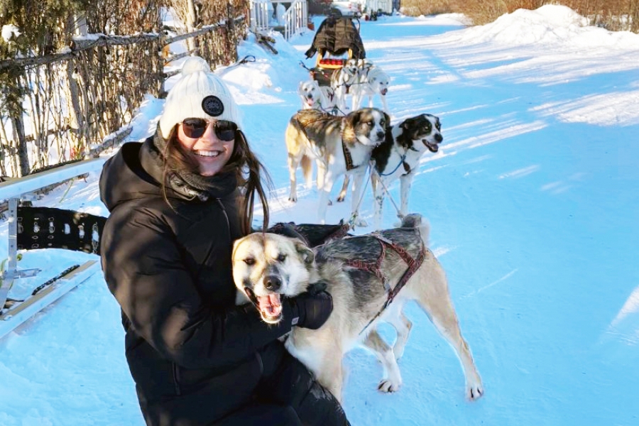 Student crouches in the snow to pet a dog.