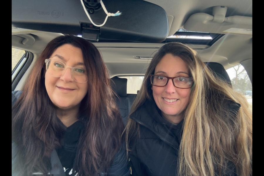 Two females in parkas sitting in the front seat of a car. 