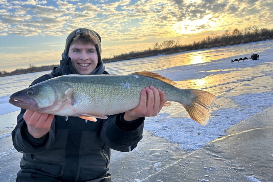 man holds fish under winter sunset