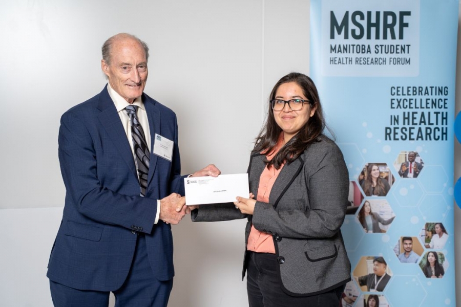 A person presenting an award to a student, behind them there's a banner that says MSHRF - Manitoba Student Health Research Forum, Celebrating Excellence in health research.