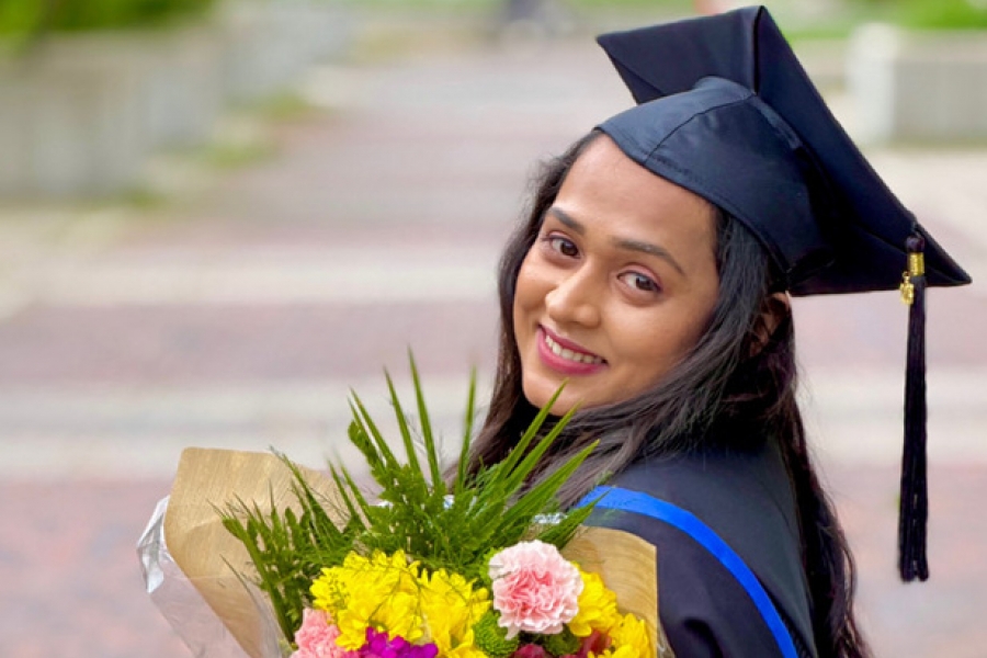 a smiling student in convocation cap and gown holds a bouquet of flowers