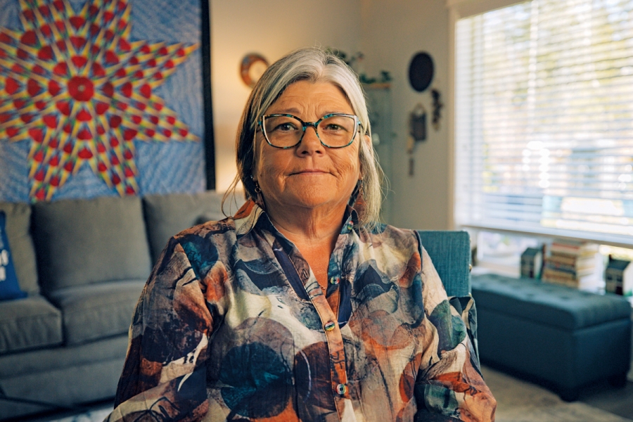 Shannon McDonald in her living room, smiling at the camera. Behind her are couches and a star blanket hangs on the wall.