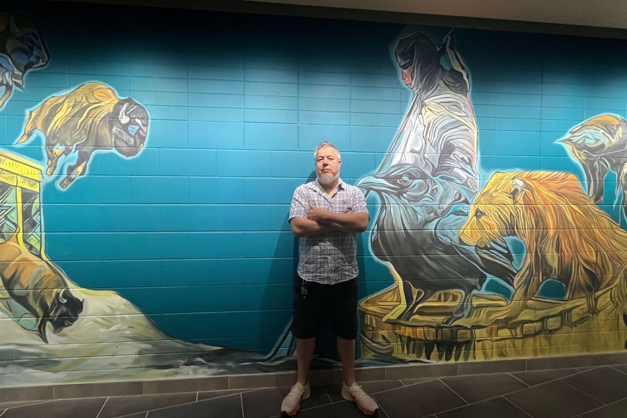 Artist stands in front of vibrant mural