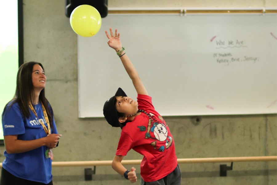 A child reaches for a balloon while being observed by an inclusion leader at a Mini U camp.