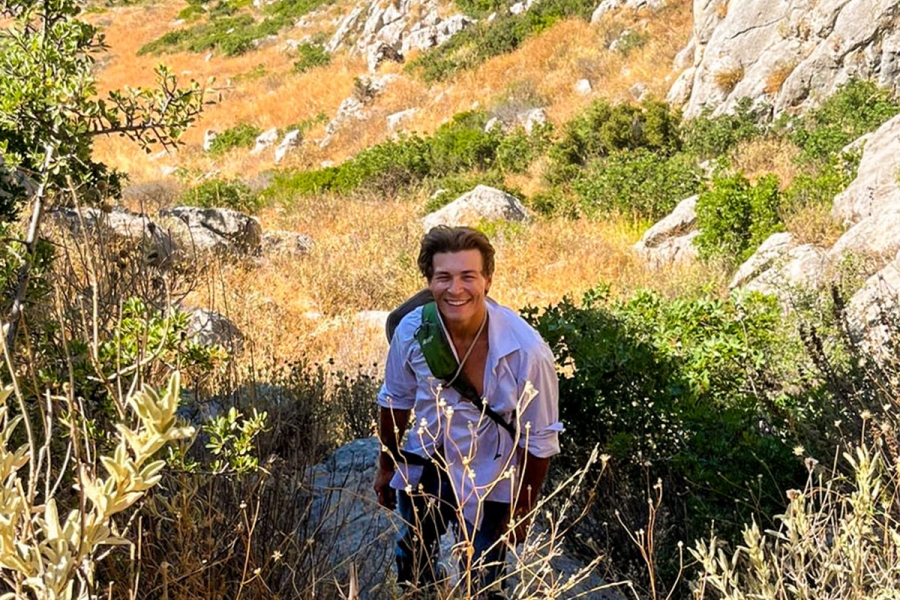 Person wearing a sling back bag, standing in a lush valley in Greece. 