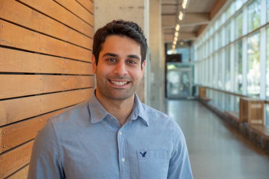 Sam Kavosh smiles warmly at the camera while standing in a hallway at the UM Apotex Centre.