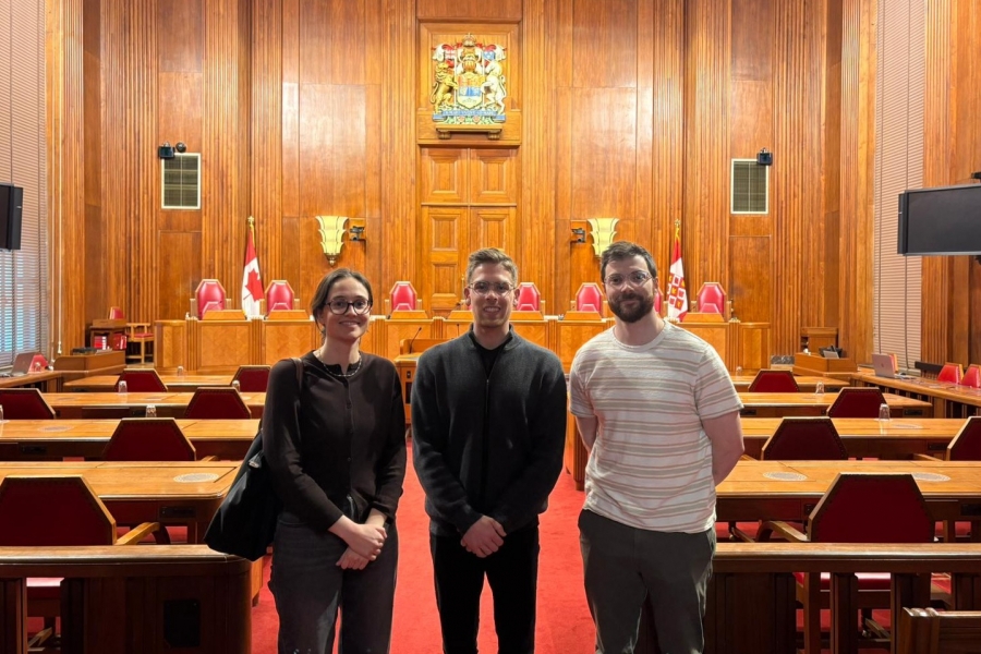 three law students in casual dress stand in a wood paneled courtroom