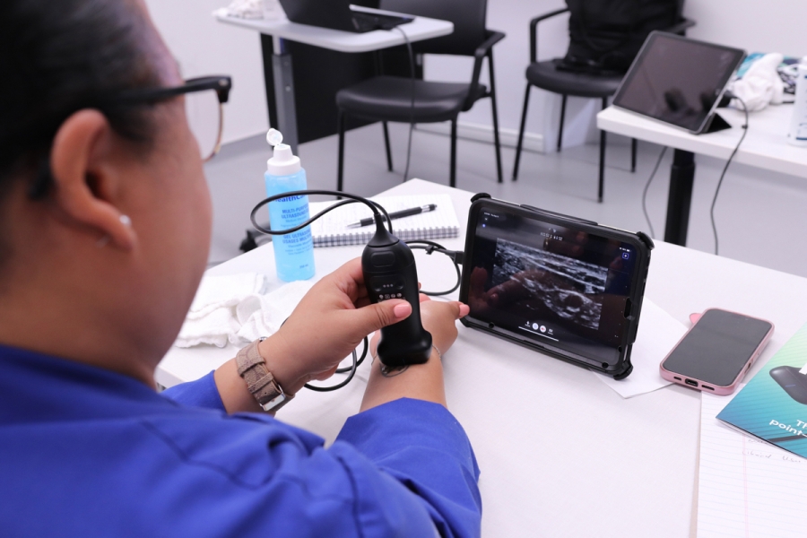 A person using a handheld ultrasound probe on their wrist, imaging is shown on a tablet.