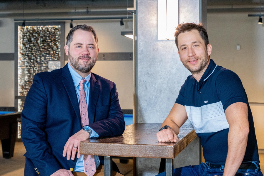 Two men sitting at a bar height table, each leaning in with their elbow on the table.