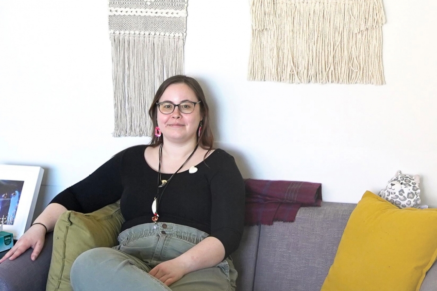 Person sits on sofa in front of decorative wall hangings.