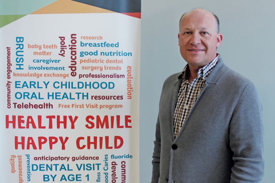 Dr. Robert Schroth stands next to a pop-up banner with words related to children's oral health.