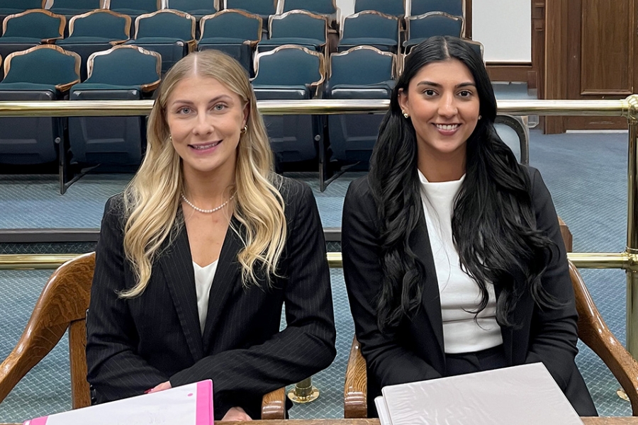 two law students in suit jackets sit at a table in a courtroom