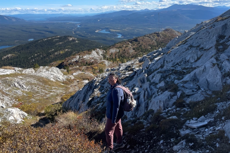 Sunjin Han hiking along a rocky trail at the peak of Grey Mountain under a clear blue sky.