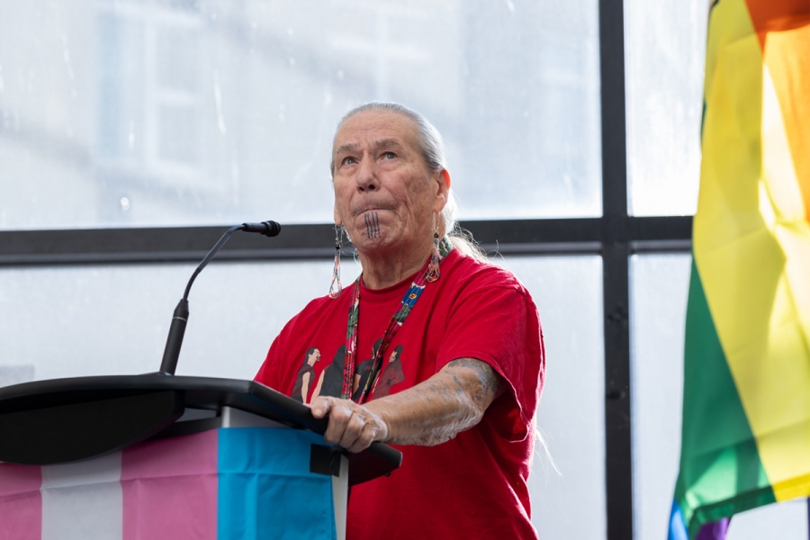 Charlotte Nolin speaks at a podium that has a trans flag hanging on front.