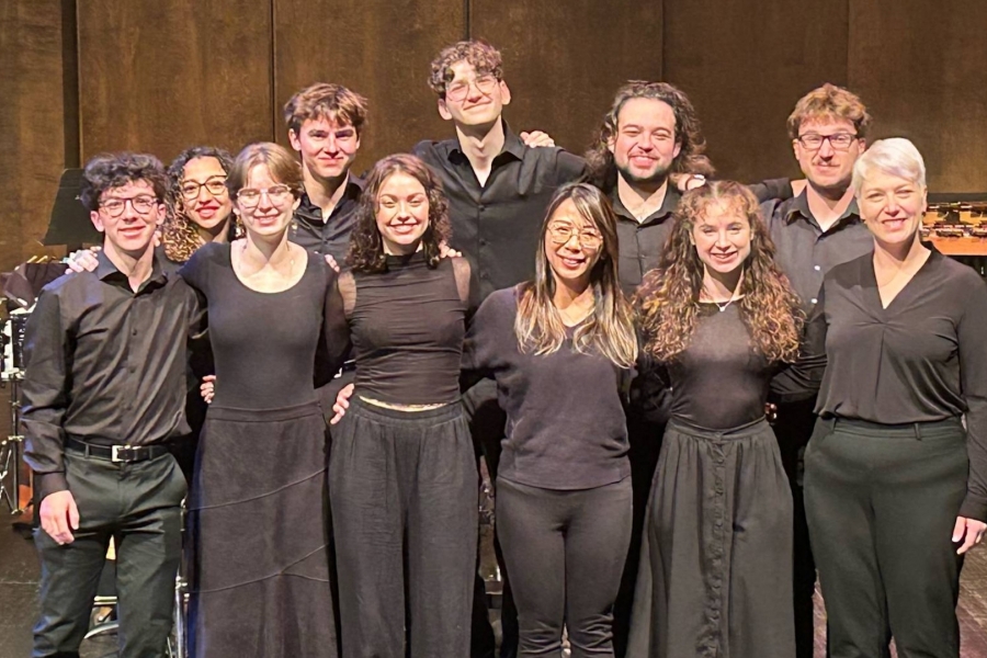 the percussion emsemble stands onstage, all dressed in black and smiling and looking at the camera.