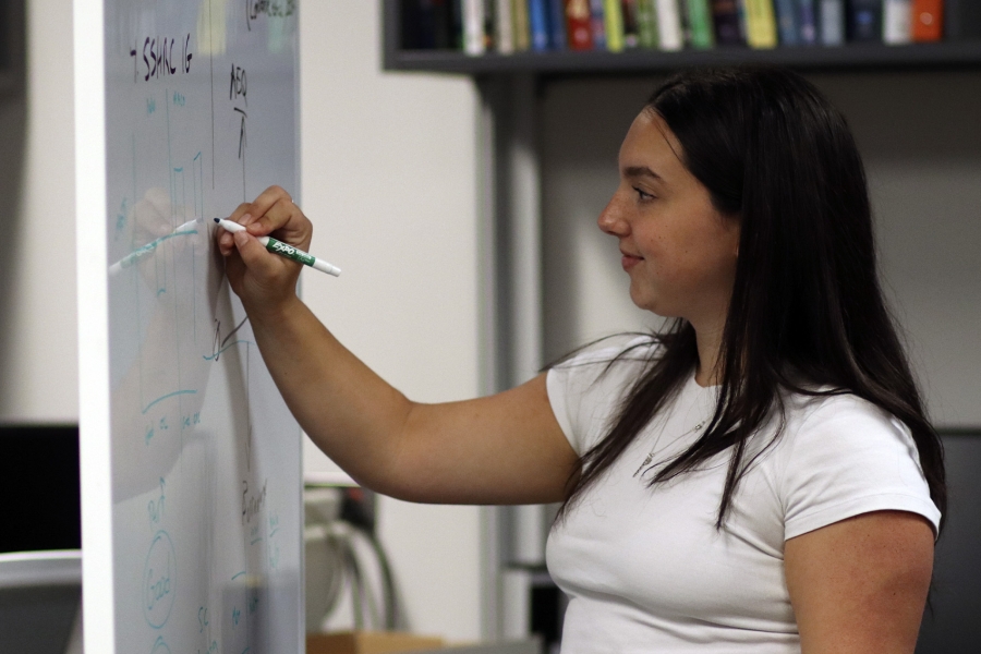 A young researcher writes on a whiteboard.