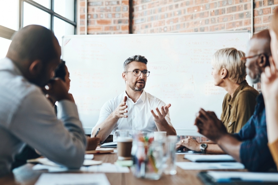 A man speaks to others seated at a boardroom table.