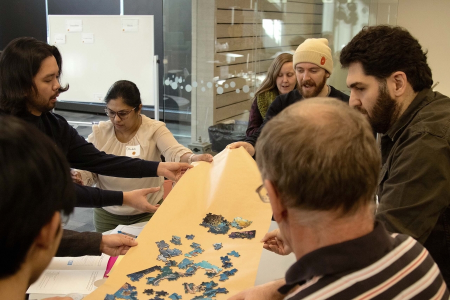 People hold a large piece of tan-coloured paper topped with bright blue puzzle pieces.