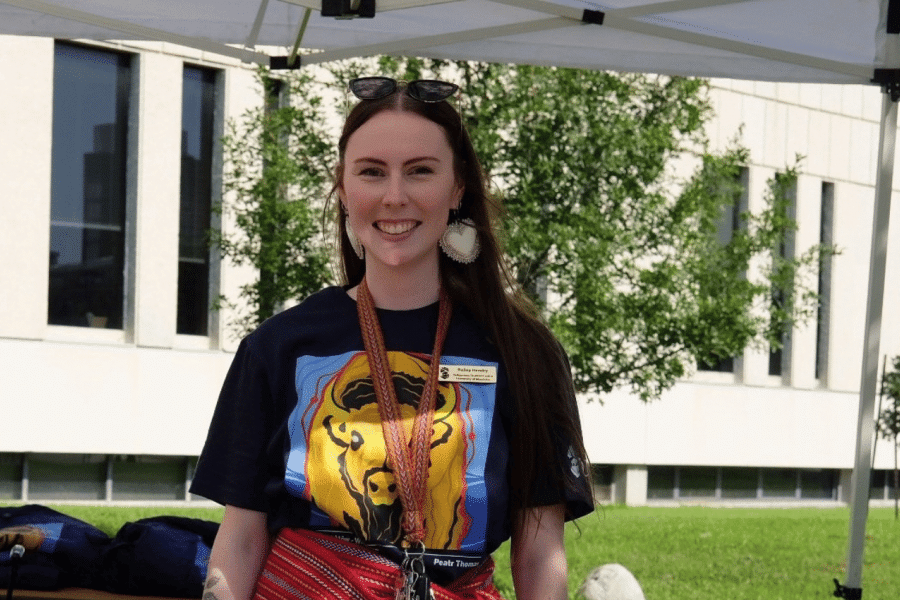 Bailey Pigeau smiles at an outdoor information table during 2025 Indigenous Orietation.