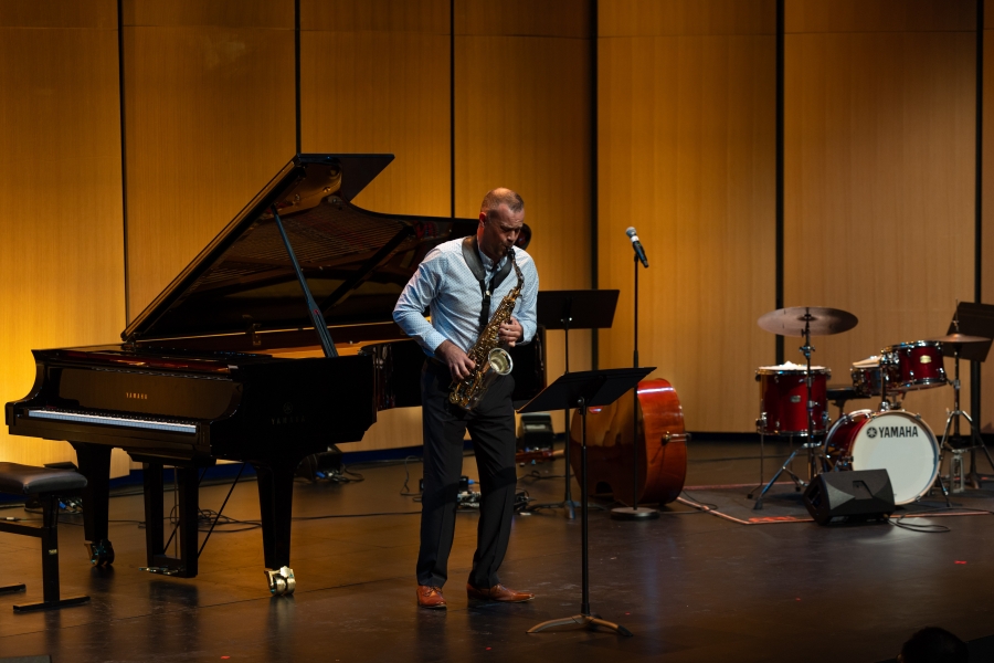 A saxophonist performs onstage with a piano, bass and drum kit.