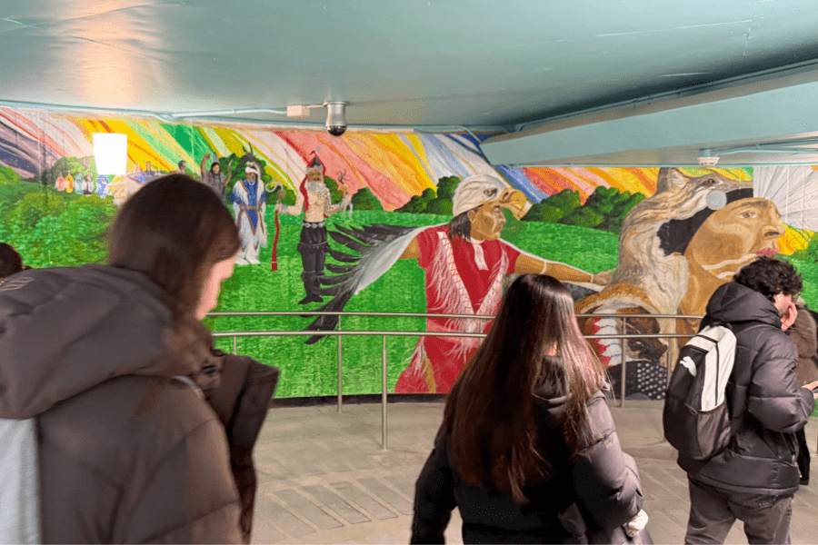 students walking past colourful Indigenous mural in tunnel system on campus.