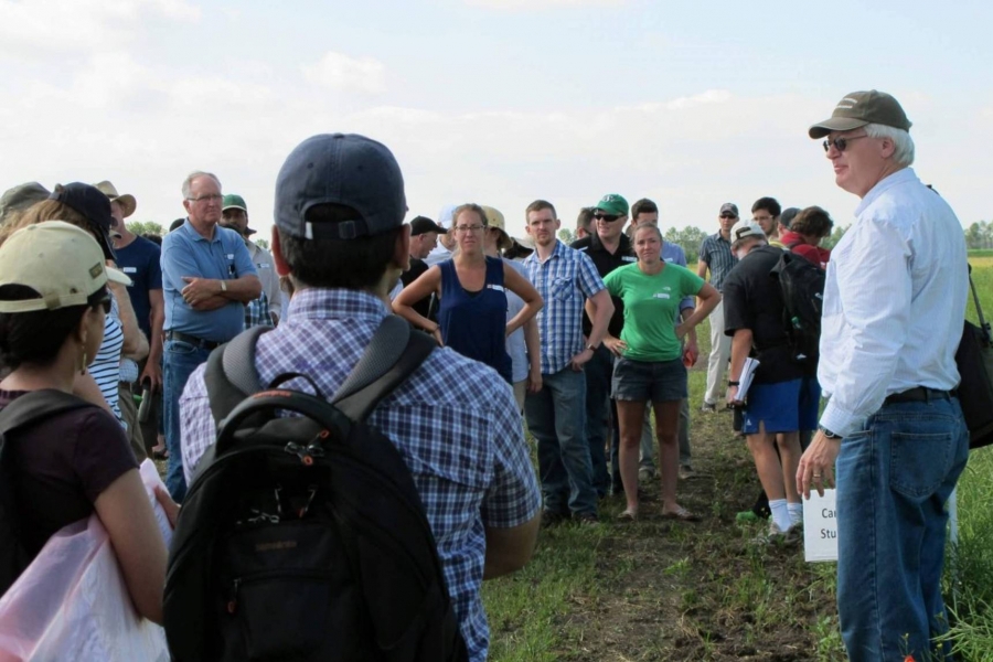 Don Flaten stands in a field surrounded by a group of people giving a lecture.