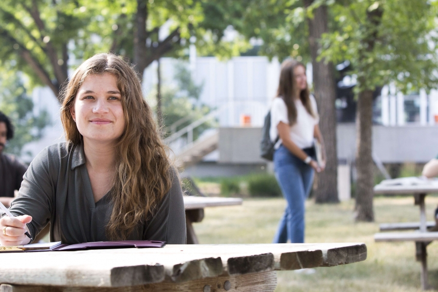 Smiling young woman sits outdoors at picnic table at Fort Garry campus.