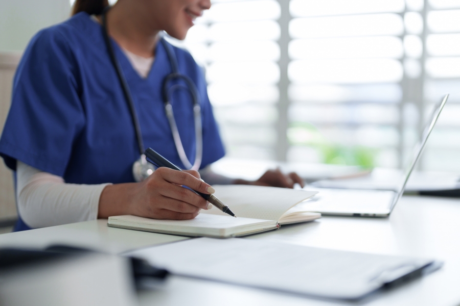 A young woman wearing medical scrubs and a stethoscope using a laptop anddoing research.