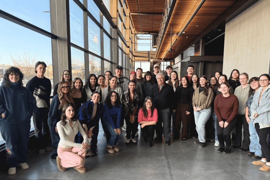 A group of Indigenous students and staff posing together in a bright indoor atrium with large windows.