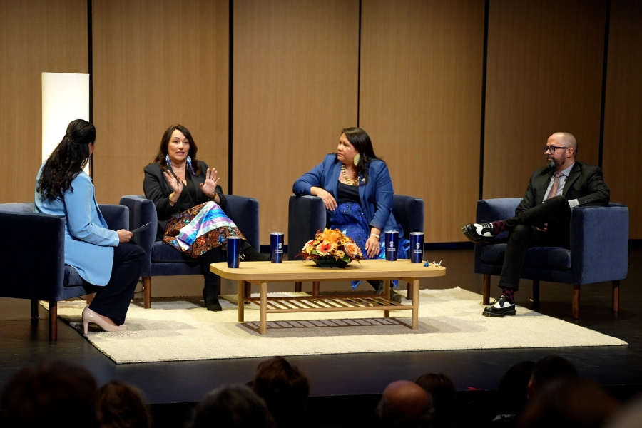 Angie Bruce, Diane Roussin, Kathleen Bluesky and Peter Pomart in conversation seated in chairs on a stage around a coffee table.