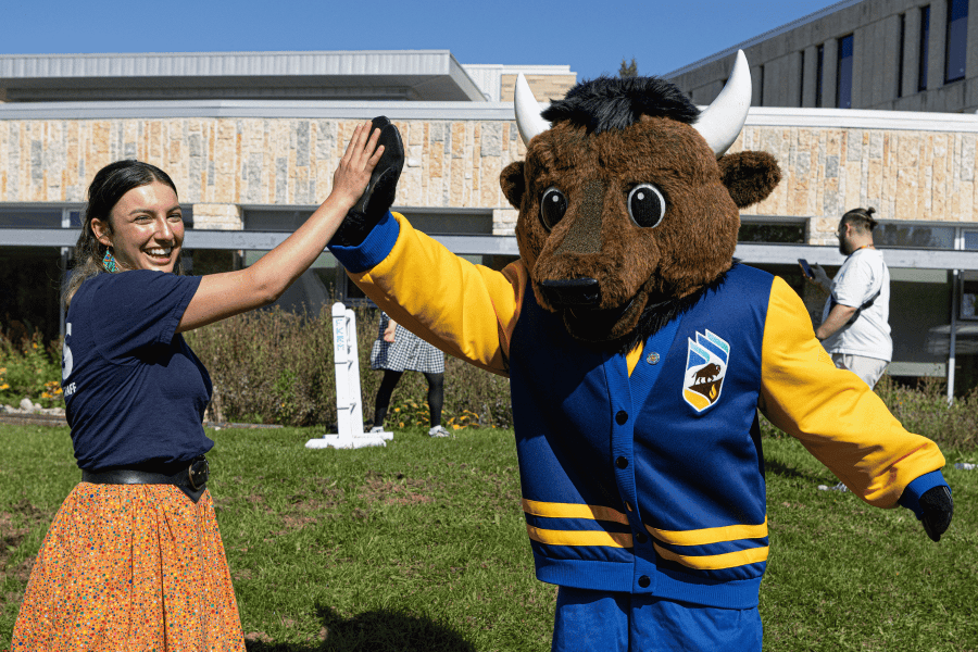 An Indigenous student high-fives the Bisons mascot outdoors.